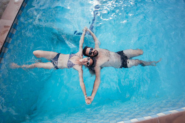 Un joven par de amantes nada en la piscina. Recién casados relajándose en el agua en la piscina al aire libre
 - Foto, Imagen