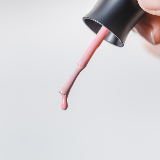 partial view of woman holding brush with pink dripping nail polish isolated on grey - Photo, Image