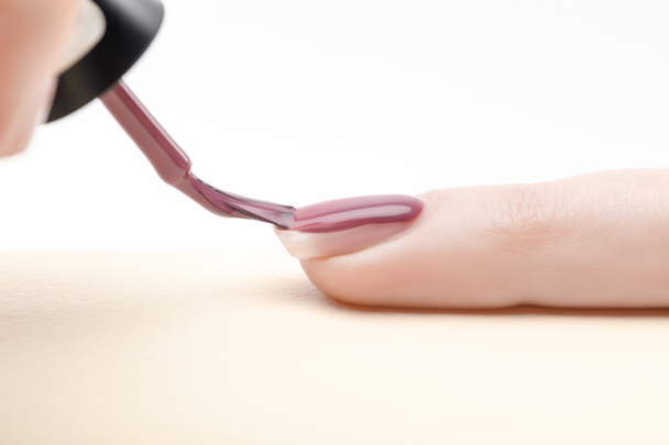 manicurist applying purple nail polish on fingernail of woman on white background - Fotó, kép