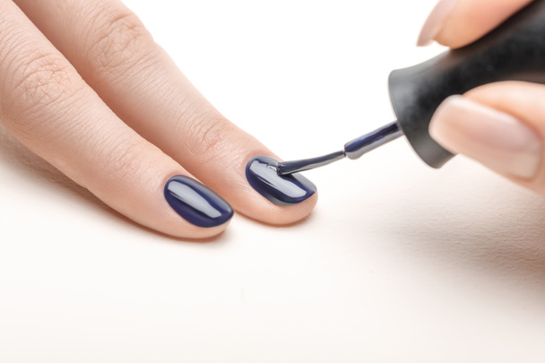 vrouwelijke manicure marine blauwe nagellak toe te passen op de vingernagel van vrouw op witte achtergrond - Foto, afbeelding
