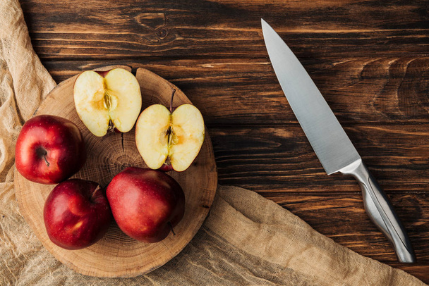 vista superior de manzanas rojas deliciosas en tocón, cuchillo y tela en mesa de madera
 - Foto, Imagen