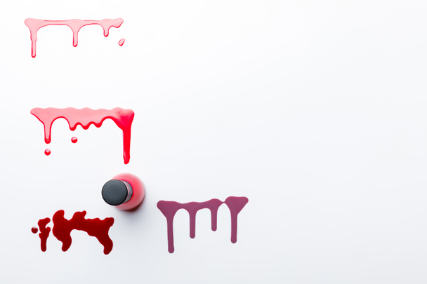 top view of bottle with red nail polish near dripping multicolored spills isolated on grey - Photo, Image