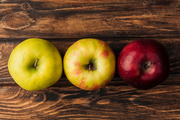 верхний вид ряда спелых разноцветных яблок на деревянный стол
 - Фото, изображение