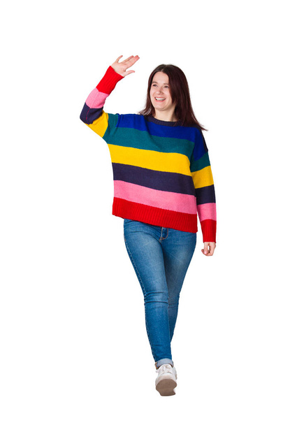 Full length portrait of carefree friendly young woman, smiling broadly while waving palm raised up, greeting friend, say hello gesture. Casual girl wearing jeans and sweater isolated over white. - Photo, Image