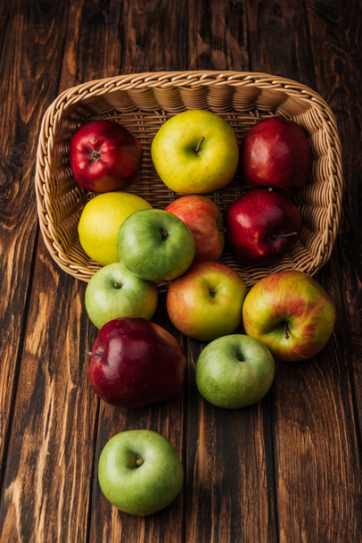 wicker basket with scattered ripe apples on rustic wooden table - Fotó, kép