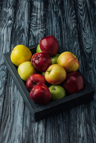 Caja de madera con manzanas maduras rojas, verdes y doradas sobre la mesa
  - Foto, Imagen