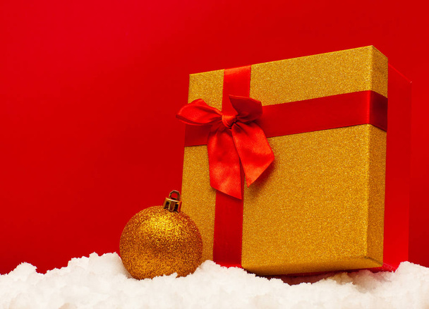 Gift and Christmas ball on snow on a red backgroun - Fotó, kép