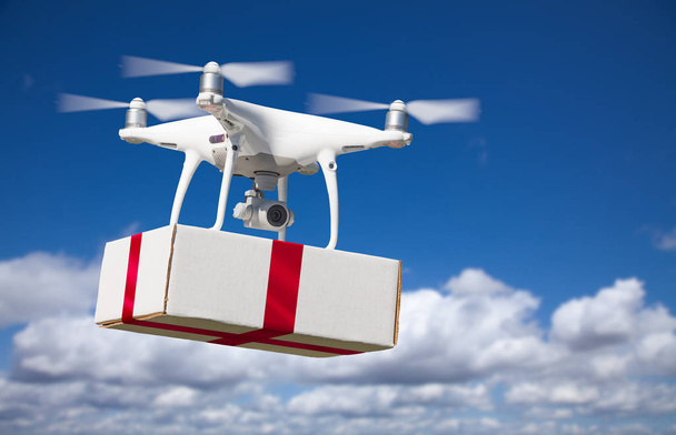 Unmanned Aircraft System (UAV) Quadcopter Drone Delivering Box With Red Ribbon - Photo, Image