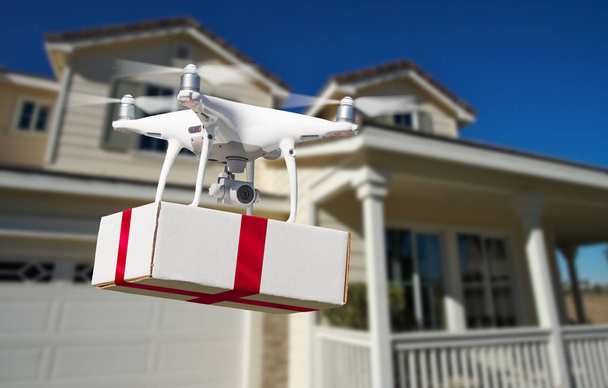 Sistema de aviones no tripulados (UAV) Quadcopter Drone entrega caja con cinta roja a casa
 - Foto, Imagen