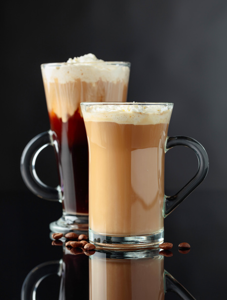 Erilaisia kahvijuomia mustalla heijastavalla taustalla. Latte ja irlantilainen kahvi lasimukeissa
. - Valokuva, kuva
