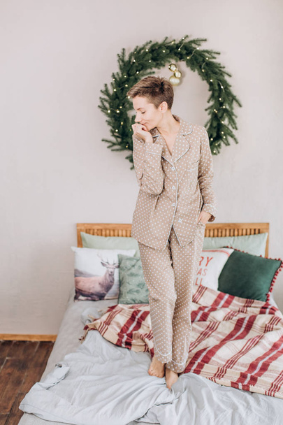 girl in pajamas in the bedroom on the bed with a Christmas wreath - Foto, afbeelding
