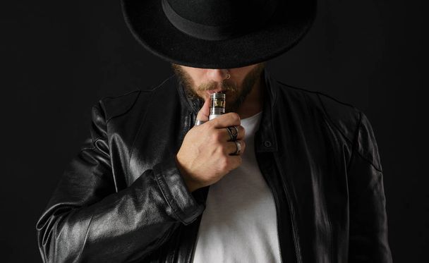 Man with vaping mod exhaling steam at black studio background. Bearded guy smoking e-cigarette to quit tobacco. Vapor and alternative nicotine free smoking concept - Foto, Imagem