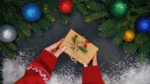 Zenske ruce dá dárek zabalený v kraftový papír ve středu rámu s větvemi jedlí a sníh a pak to bere. Vánoční dekorace - girlanda světýlky, ozdoby - Záběry, video