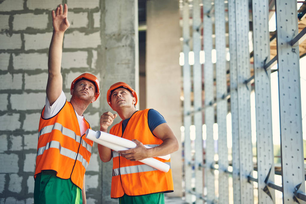 Thoughtful builder pointing to the ceiling while standing with coworker - 写真・画像