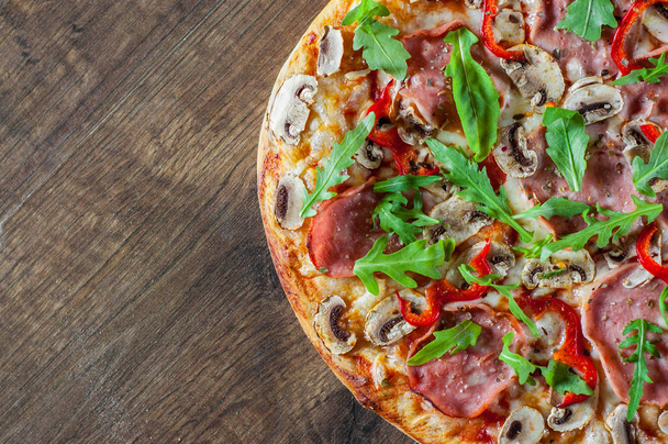 Pizza with Mozzarella cheese, mushrooms, ham, tomato sauce, salami, pepper, Spices and Fresh arugula. Italian pizza on wooden table background - Photo, Image