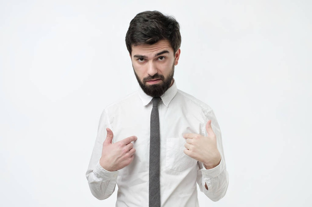 Knappe fronsend Spaanse man met dikke haren en baard wijzende vingers op zichzelf - Foto, afbeelding
