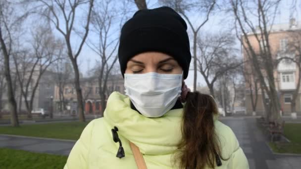 Молодая женщина стоит на улице в защитной медицинской маске и защищена от вирусов зимой
. - Кадры, видео