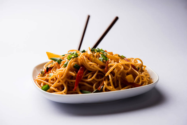 Schezwan 麺の客家麺や焼きそばの野菜は木の箸を添えてボウルやプレート人気のインド-中国語レシピです。選択と集中 - 写真・画像
