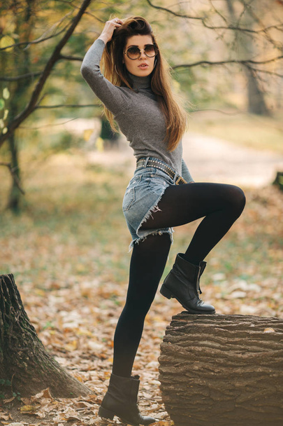 Photo of woman in sunglasses standing by log in autumn park - Photo, Image