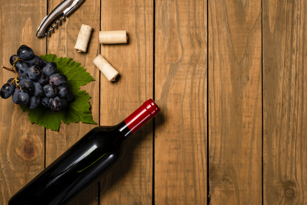 Garrafa e copo com cachos de vinho de uvas e folhas de videira em fundo de madeira. Vista superior com espaço de cópia
. - Foto, Imagem
