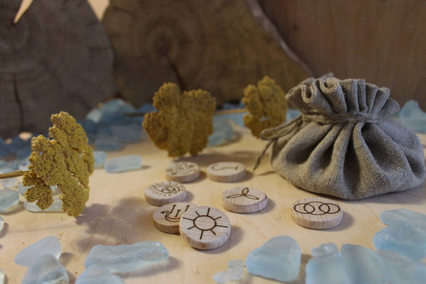 Runas de bruja hechas a mano de madera con una bolsa de lino, cristales azules y flores amarillas en un estilo rústico
 - Foto, Imagen