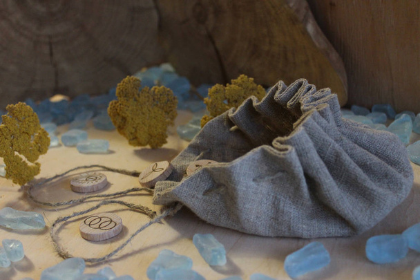 Houten handgemaakte heks runen met een linnen zakje, blauwe kristallen en gele bloemen in een rustieke stijl - Foto, afbeelding