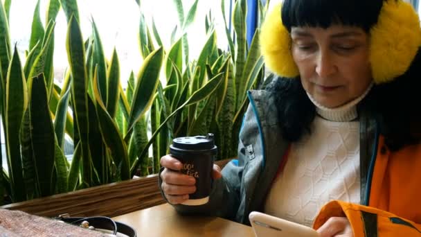 Hermosa mujer de negocios adulta con su teléfono inteligente tomando café en la cafetería, sentada junto a la ventana. Primer plano
 - Imágenes, Vídeo