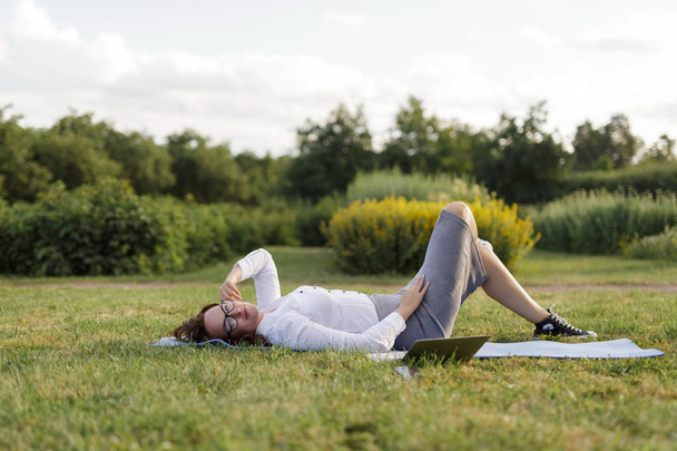 Beautiful big girl lying on the green grass in park with her laptop and relaxing. - Foto, Imagem