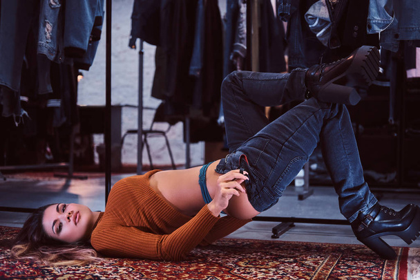 Sexy dziewczyna uwodzicielsko ciągnąc się spodnie, leżąc na podłodze w przymierzalni sklepu z odzieżą. - Zdjęcie, obraz