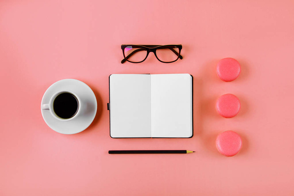 Coffee, macaron, clean notebook, eyeglasses and flower on living coral table from above. Female working desk. Flat lay style. - Foto, imagen