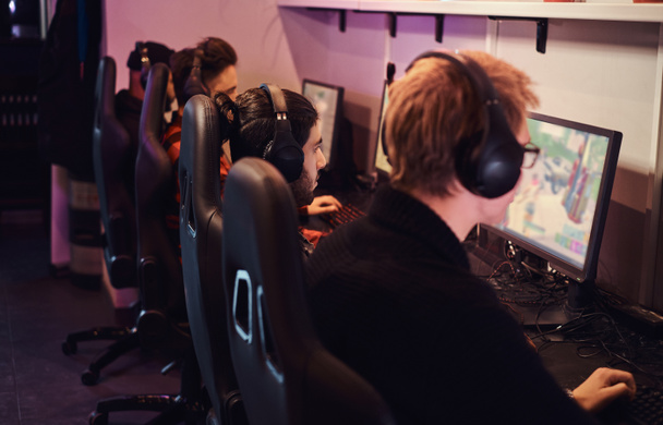 Un equipo de deportistas cibernéticos profesionales, entrenados para el campeonato, juega en un videojuego multijugador en PC en un club de juegos o cibercafé
. - Foto, Imagen