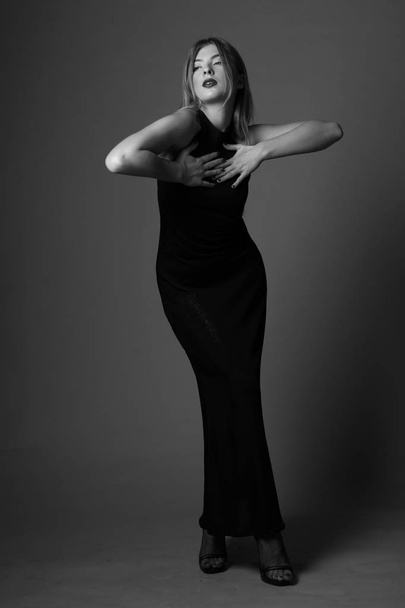 Cute blonde woman in gorgeous, elegant dress.Posing on grey backgorund.Black and white.Studio. - Zdjęcie, obraz