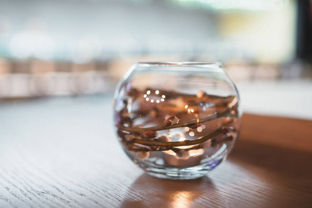 Round glass vase with a sprig of willow inside on a table in a restaurant - Photo, Image
