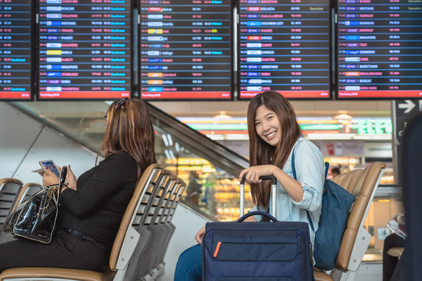 Azjatycki podróżnik z bagażem z paszportu siedzącego nad pokładzie samolotu do odprawy na ekranie informacyjnym lotu w nowoczesnym lotnisku, podróży i transportu z koncepcją technologii. - Zdjęcie, obraz