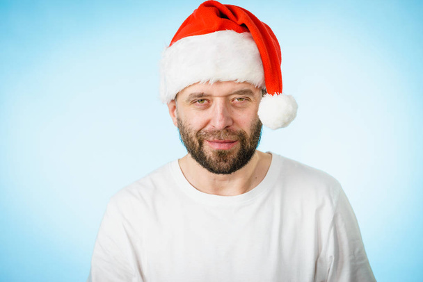Bearded man wearing santa claus hat portrait, on blue with copy space. Christmes time. - Photo, Image