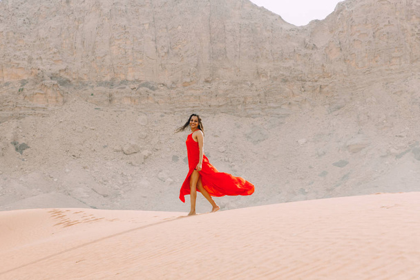 Young beautiful Indian woman in red dress walking in the desert with mountains - Zdjęcie, obraz