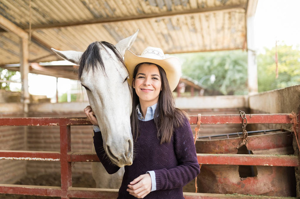 Retrato de vaquera sonriente y caballo blanco de pie en el rancho
 - Foto, Imagen