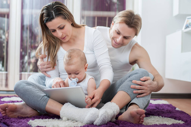 Happy parents sitting on the floor and playing on tablet with their baby boy - 写真・画像