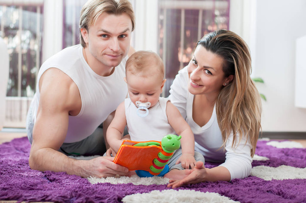 Happy parents laying down on the floor and playing with their baby boy. - Zdjęcie, obraz