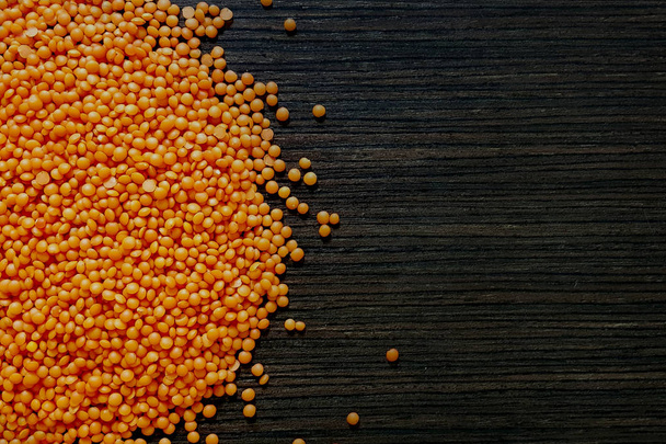 Red lentil is poured on a wooden background with a copyspace. - Photo, Image