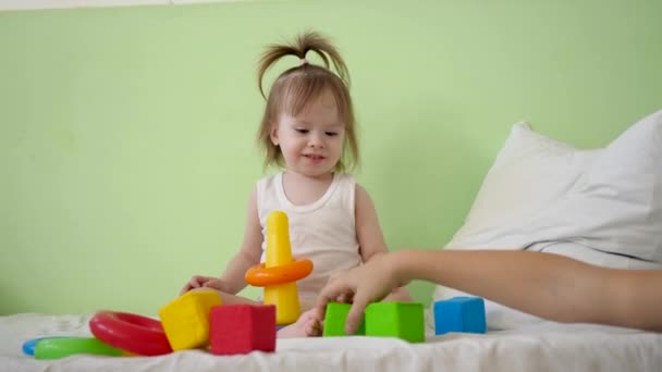 moeder en kind spelen met kleurrijke kubussen op bed. Educatief speelgoed voor kinderen van voorschoolse en kleuterschool. Speelgoed voor jong geitje. kind speelt in de kamer op het bed met kubussen en bouwt de toren met moeder - Video