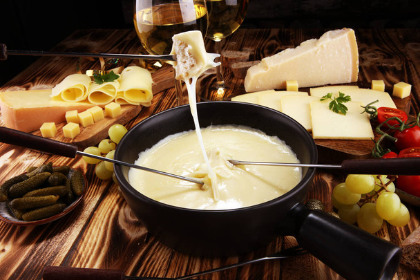 Bir kış akşamında gurme İsviçre fondü yemek peynir fondü iki çatal bir lokali veya restoran arkasında ekmek ve beyaz şarap daldırma ile ısıtmalı bir sürahi yanında bir gemide çeşitli peynir ile - Fotoğraf, Görsel