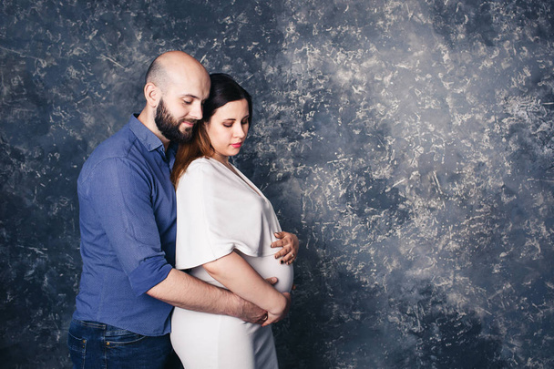 bearded man holding his pregnant wife by belly on abstract background. - Foto, imagen