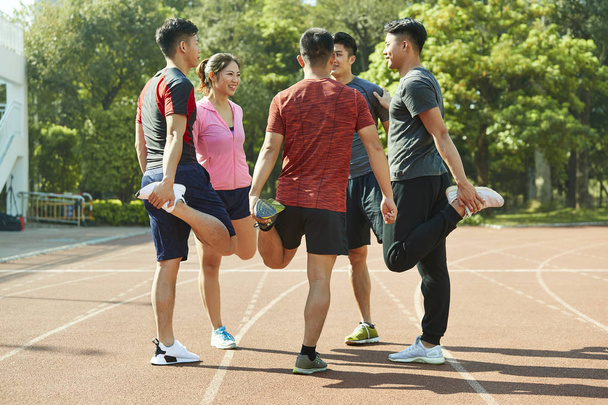 Gruppe junger asiatischer Athleten streckt die Beine auf der Strecke und bereitet sich auf das Training vor. - Foto, Bild