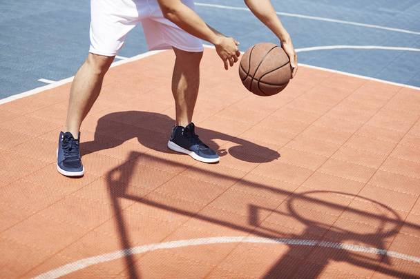 young asian male basketball player practicing ball handling skills on outdoor court. - 写真・画像