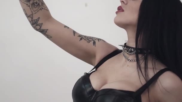 Sexy young attractive woman with aggressive makeup, big sensitive red lips, blue eyes, leather collar, earrings and long hair wearing leather clothes is pouring liquid on her body. - Footage, Video
