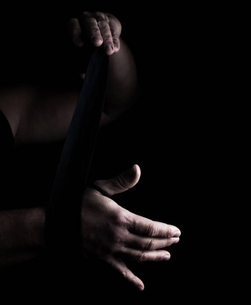 Mann wickelt seine Hände in schwarze Textilbinde für den Sport, schwarzer Hintergrund - Foto, Bild