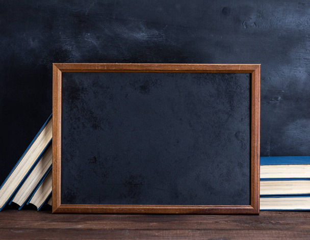 empty black chalk drawing frame and stack of books on a brown wooden table - Foto, imagen
