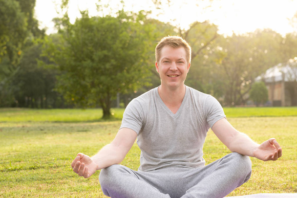 Happy pohledný mladík s úsměvem při meditaci v parku - Fotografie, Obrázek
