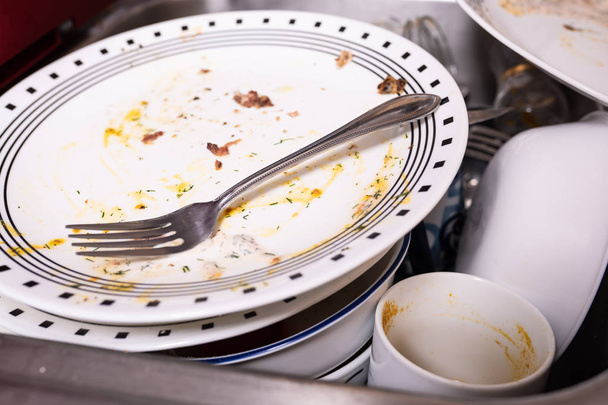 Pile of dirty dishes in the sink. Plate with a fork on top with leftovers of eggs and bacon. - Photo, Image